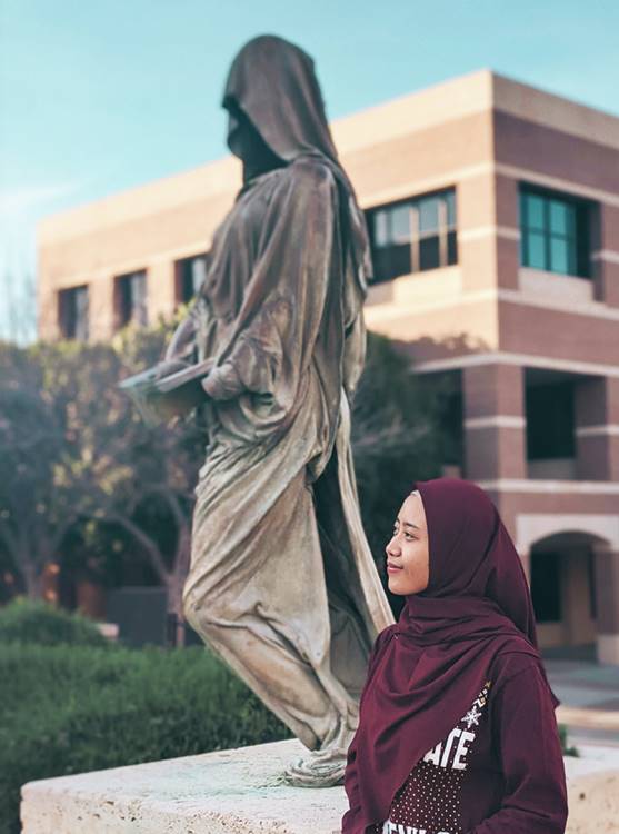 Graduate student looking towards the future in front of the statue called The Reader, sharing its spirit of knowledge.